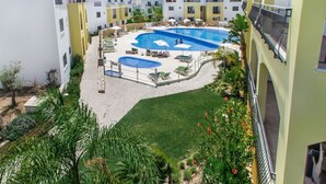 Un área de piscina en la azotea con varias piscinas, sillones de descanso y una pequeña zona verde.