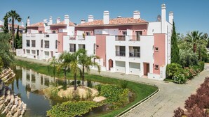 Una hilera de edificios modernos de varios pisos con balcones, una fuente central con nenúfares y un sendero pavimentado.