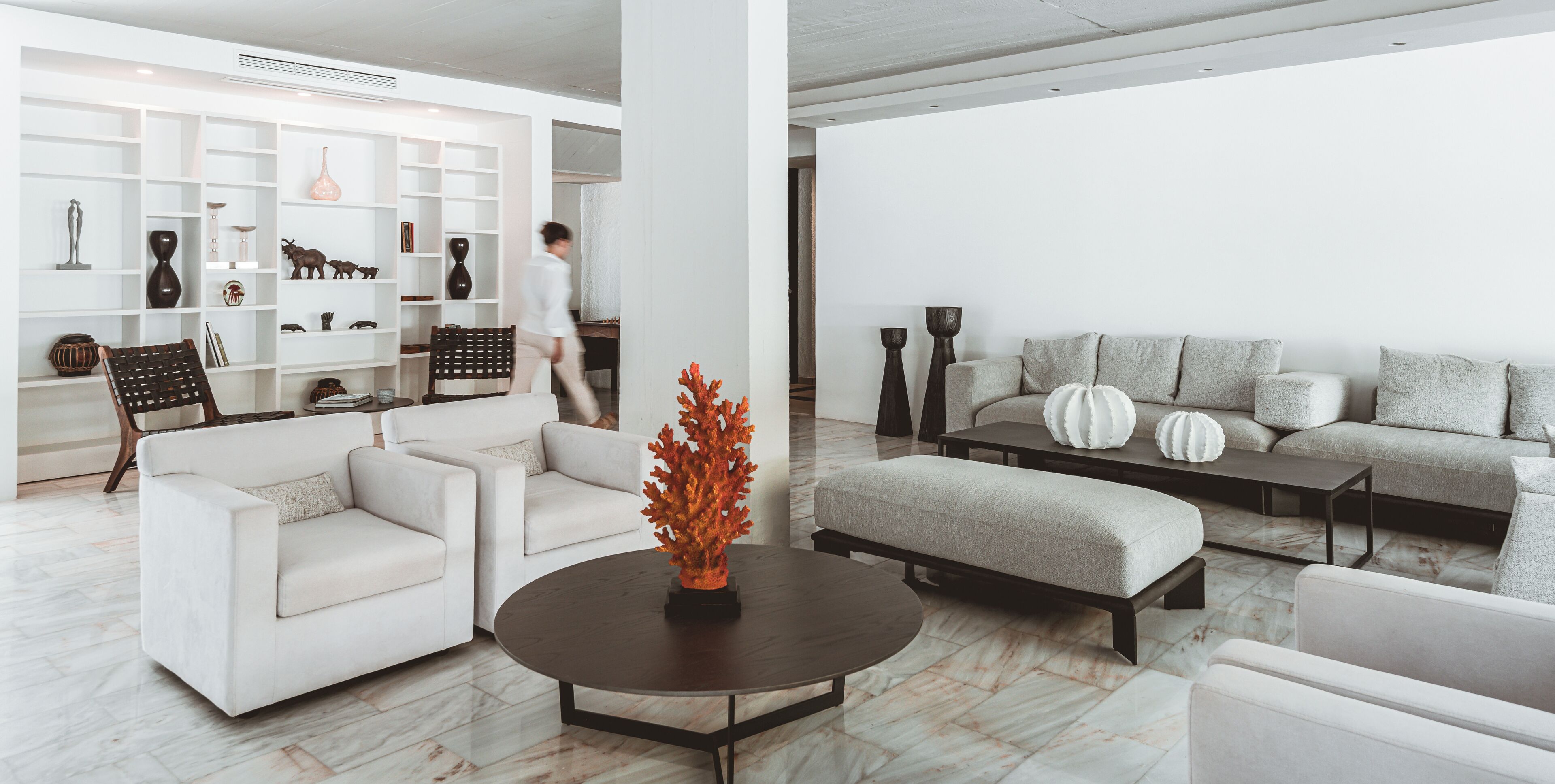 A modern living room with a white sofa, a round coffee table, and a bookshelf filled with decorative items.