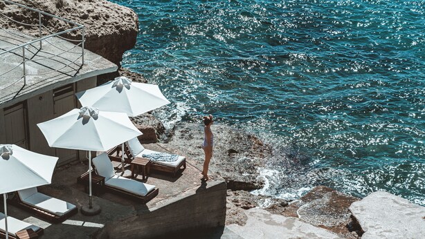 Terraza frente al mar con sillones de descanso y sombrillas.