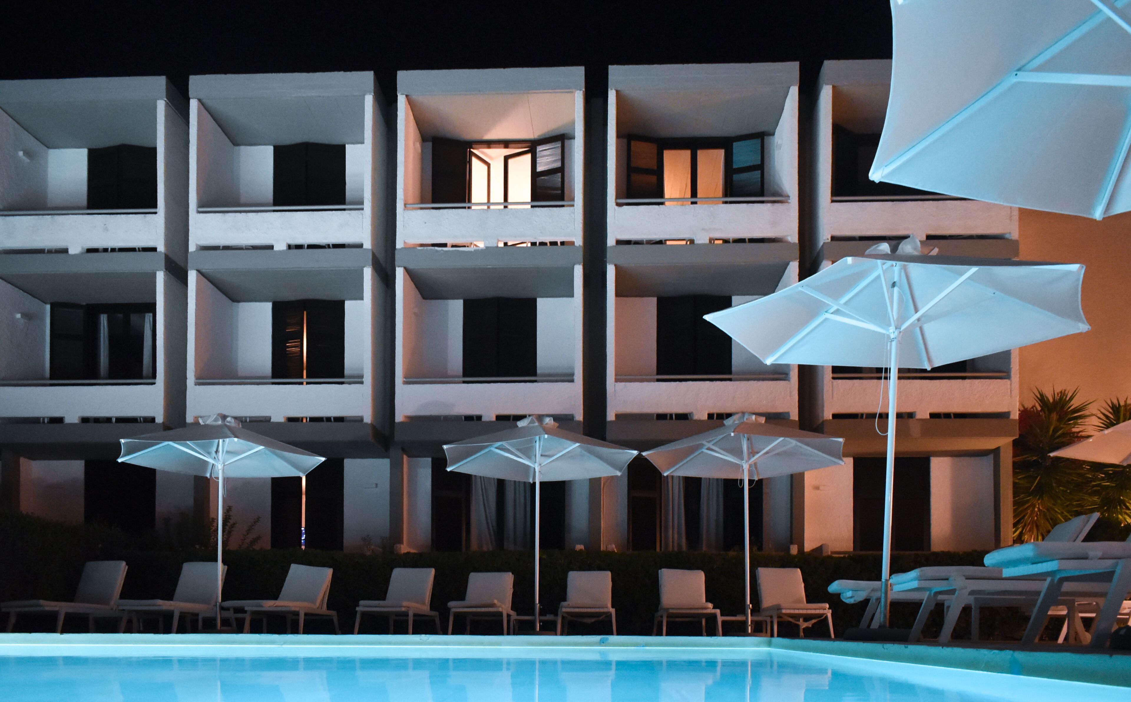 A multi-story hotel with a swimming pool, outdoor umbrellas, and lounge chairs.