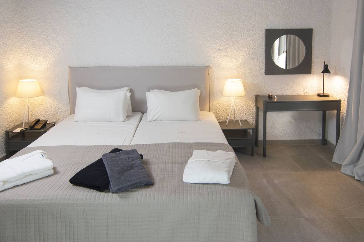 A hotel room with a double bed, two bedside tables with lamps, a bedside phone, a small table with a lamp, and a mirror on the wall.