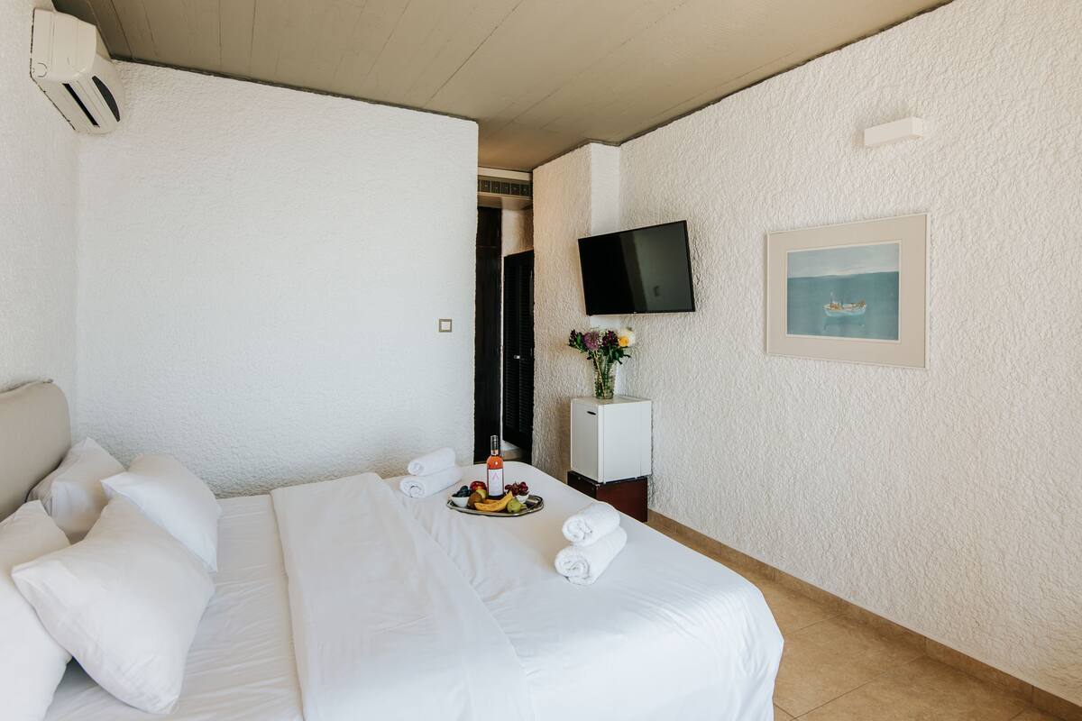 A hotel room with a bed, a TV mounted on the wall, a small cabinet, and a framed picture.