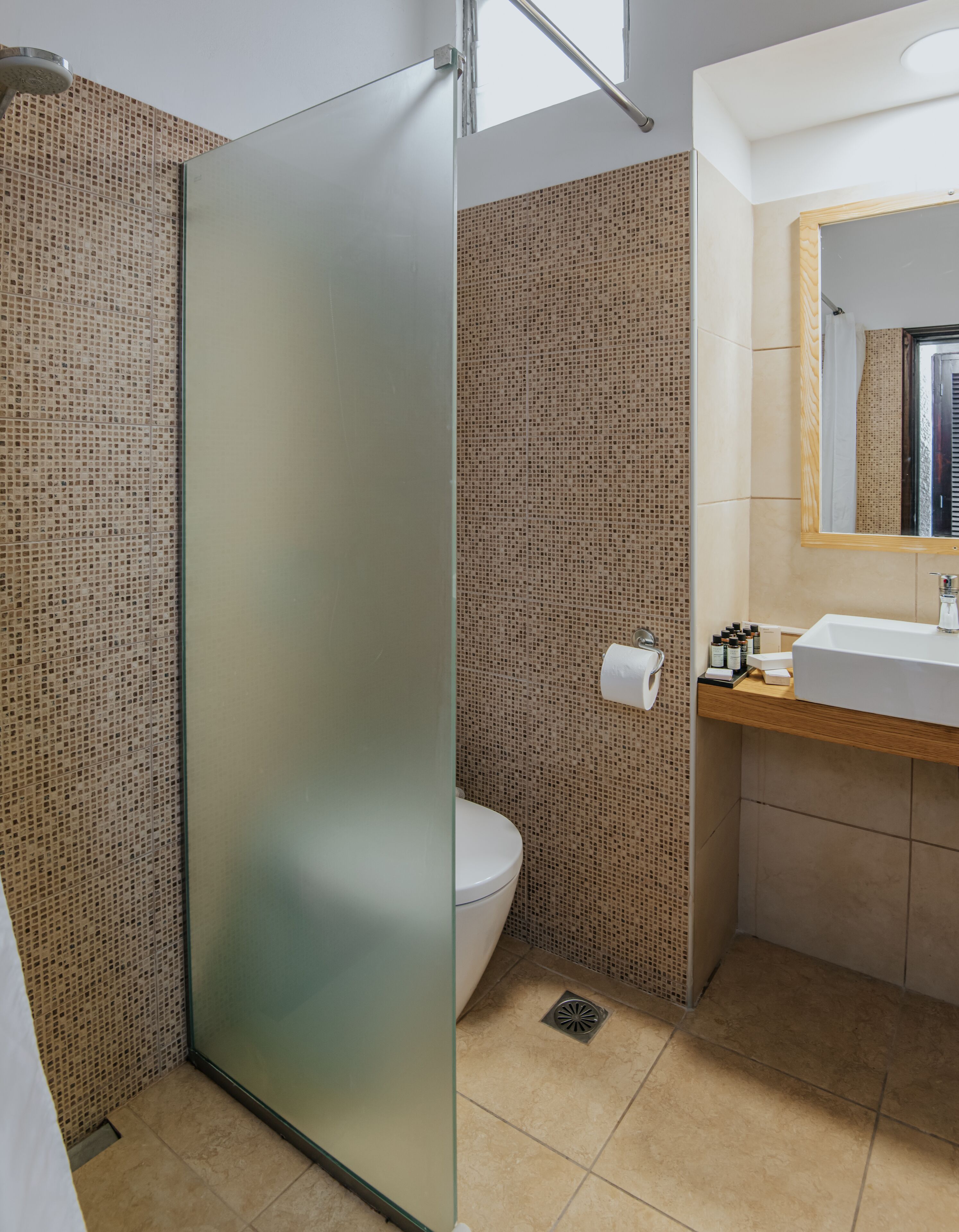 Un baño moderno con mampara de cristal, inodoro y lavamanos con artículos de aseo.
