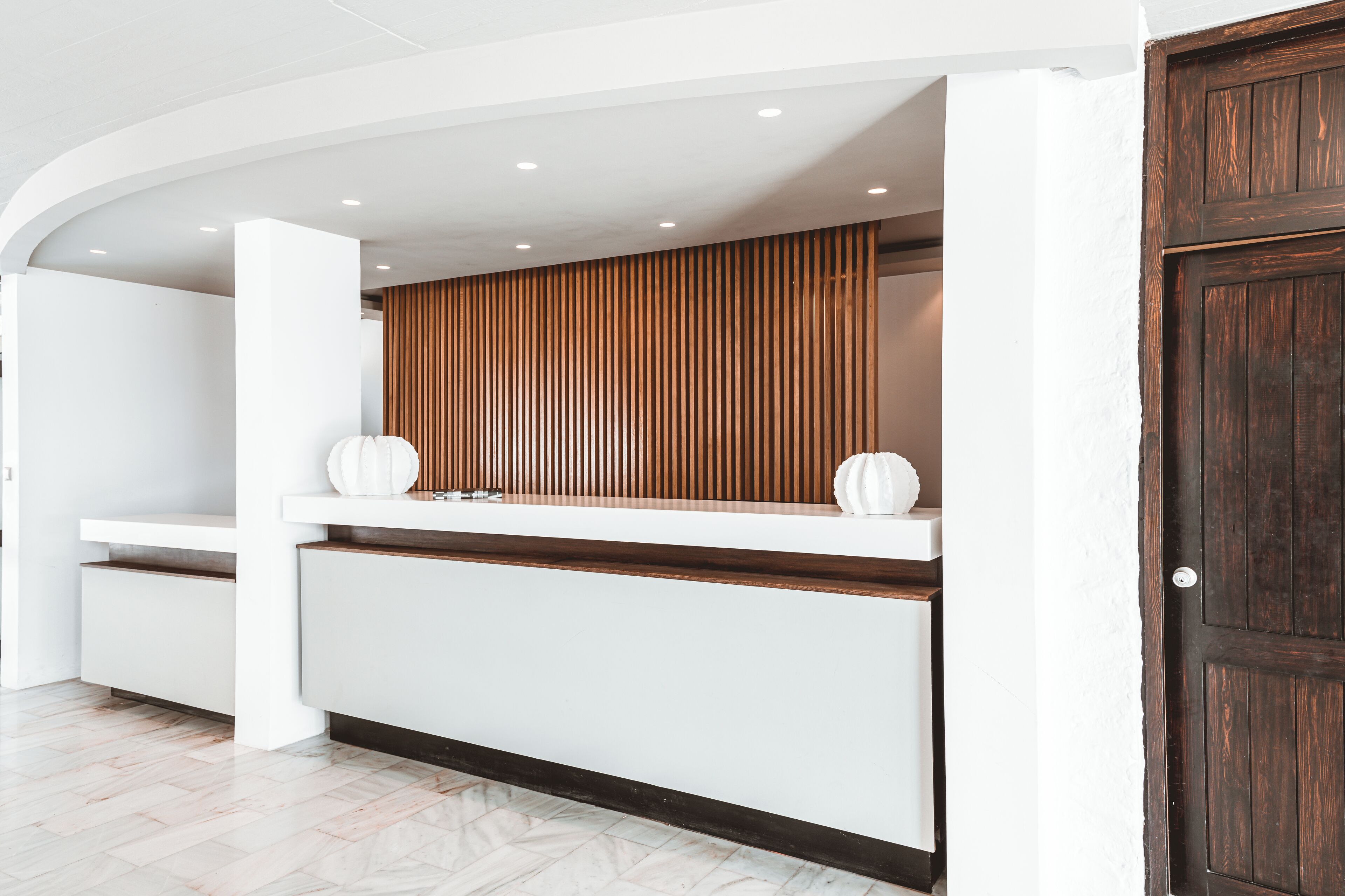 Un mostrador de recepción con diseño blanco y de madera, un panel de pared de listones de madera y una puerta de madera oscura.