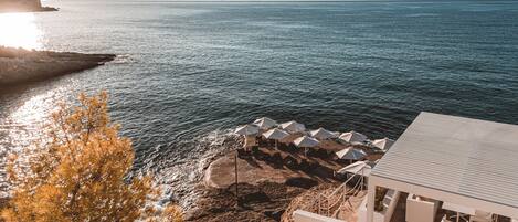 A coastal view with a beach area featuring umbrellas and outdoor seating, overlooking the sea.