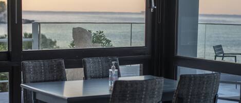 A dining area with a table and chairs, large windows with a view of the sea, and a glass door leading outside.