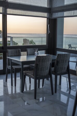 Een eetruimte met een tafel en stoelen, grote ramen met uitzicht op zee en een glazen deur naar buiten.