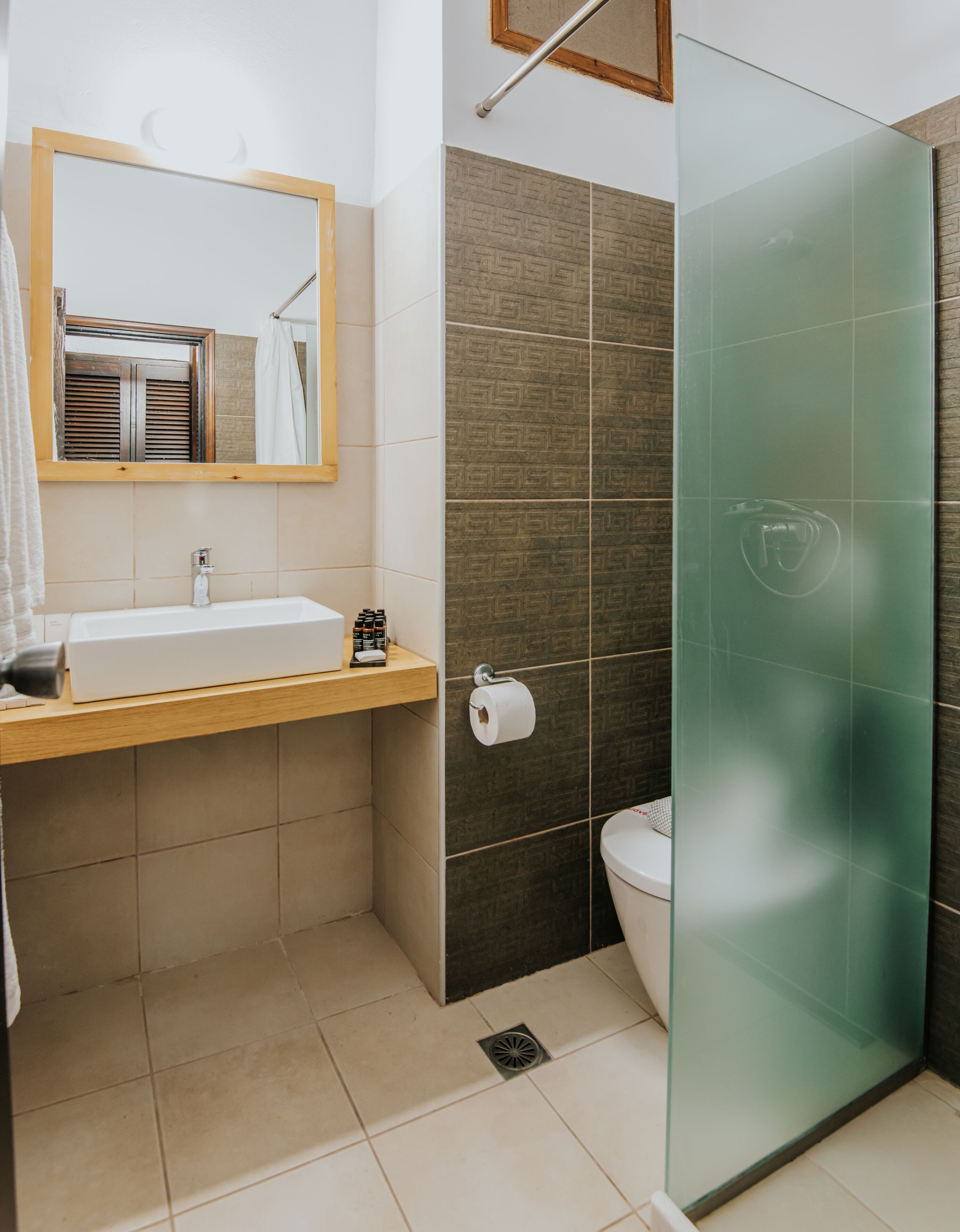 Une salle de bain avec un meuble-lavabo en bois, un miroir, des toilettes et une cabine de douche en verre.