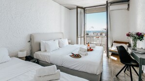 Habitación de hotel con dos camas, un escritorio con silla, vista al mar y balcón con mobiliario exterior.