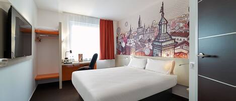 Habitación de hotel con cama, escritorio, silla y un mural de paisaje urbano en la pared.