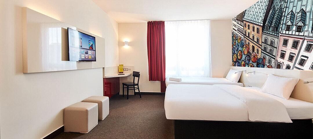 A hotel room with a bed, a desk, a chair, and a TV.