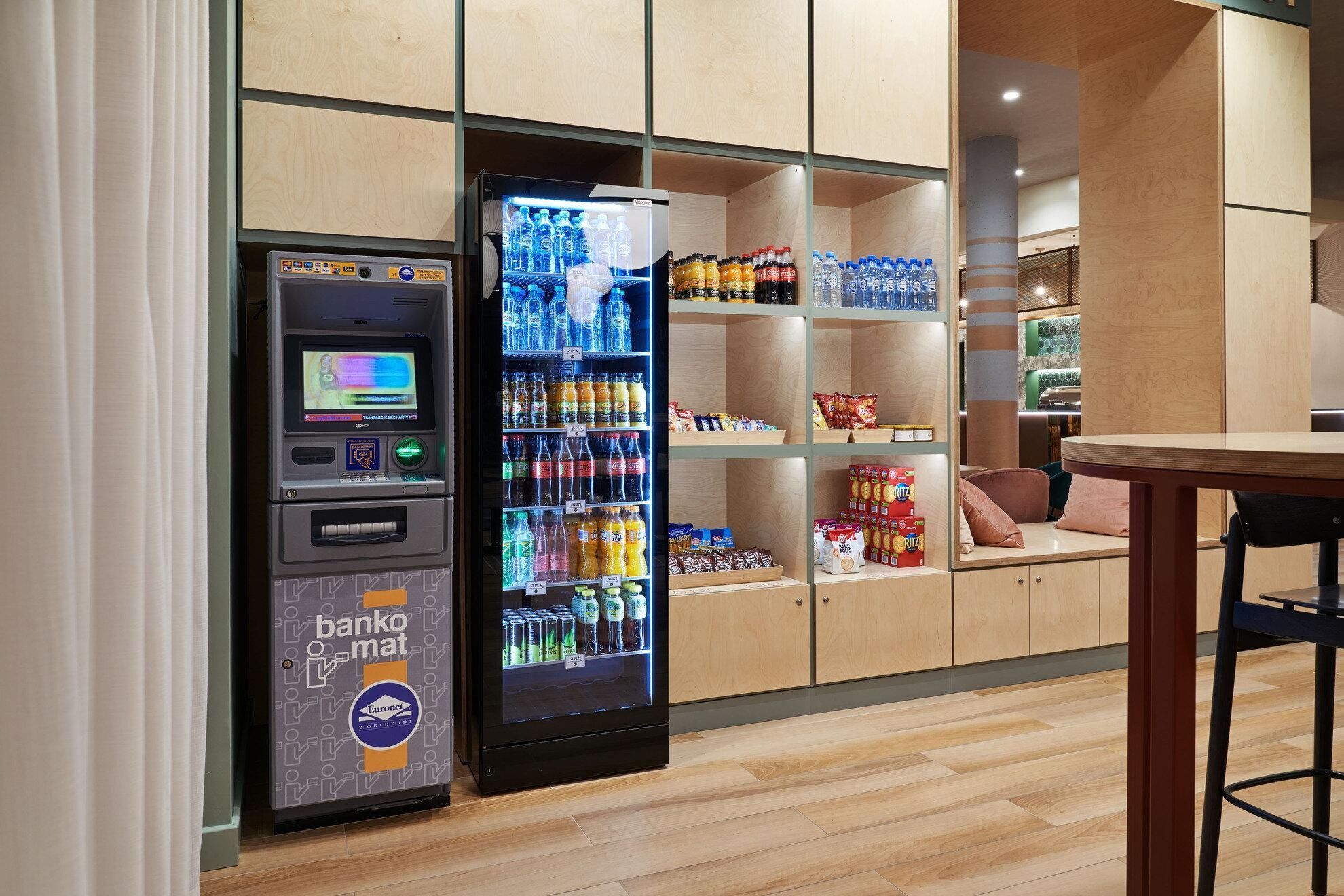 A bank ATM and a beverage vending machine in a modern interior with wooden shelving and a wooden floor.