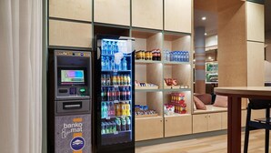 Un cajero automático y una máquina expendedora de bebidas en un interior moderno con estanterías y suelo de madera.