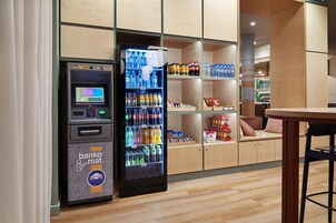 Um caixa eletrônico do banco e uma máquina de venda automática de bebidas em um interior moderno com estantes e piso de madeira.
