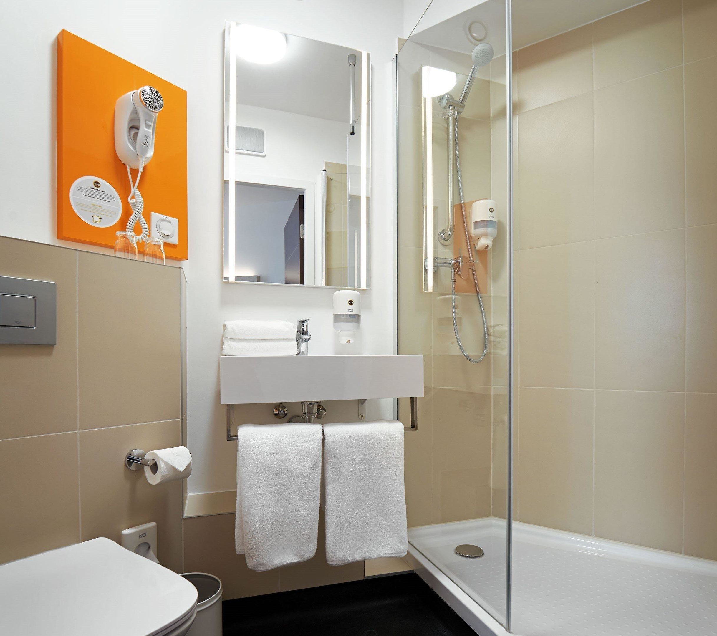 A bathroom with a shower, a sink, and a mirror. There is a towel rack with two towels.