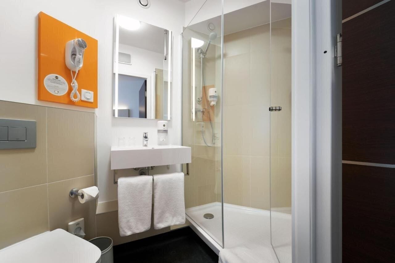 A modern bathroom with a glass shower enclosure, a white sink, and a hairdryer mounted on an orange panel.