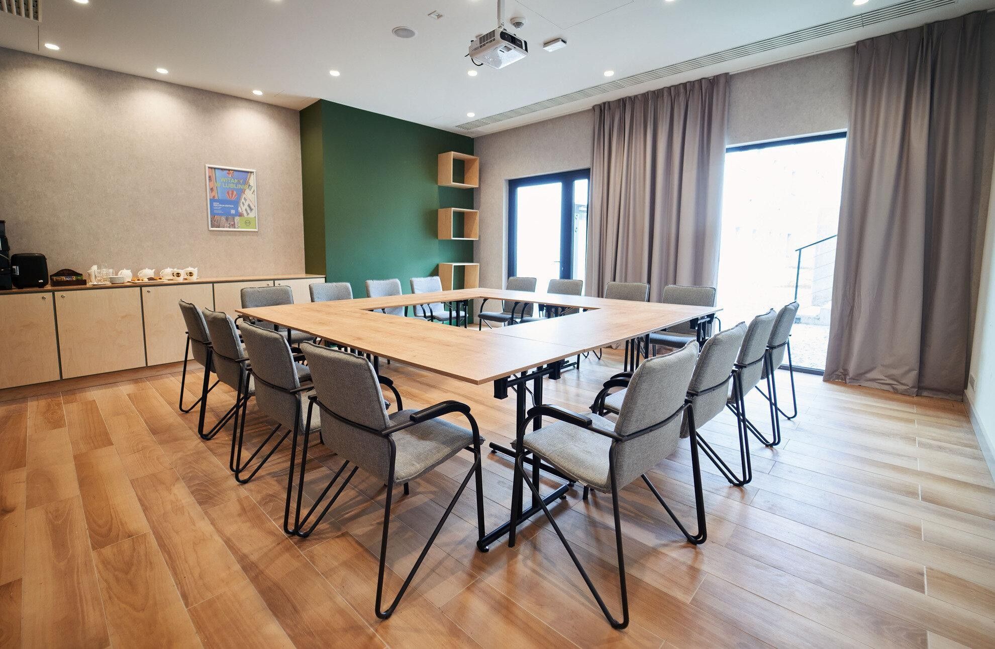 A conference room with a large table, chairs, a kitchenette, and a large window with curtains.