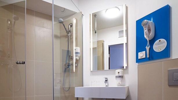A modern bathroom with a glass-enclosed shower, a white sink, and a blue towel rack. - B&B Hotel Lublin Centrum (Lublin)