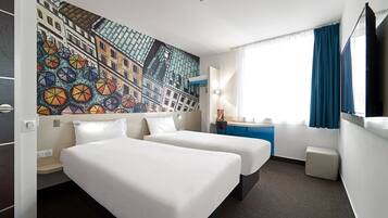 Habitación de hotel con dos camas, un escritorio, una silla, un ventanal con cortinas y un mural en la pared.