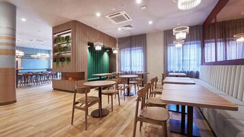 Un interior de restaurante moderno con suelo de madera, mesas redondas y una pared de acento verde.