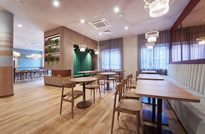 A modern restaurant interior with wooden flooring, round tables, and a green accent wall. - B&B Hotel Lublin Centrum (Lublin)