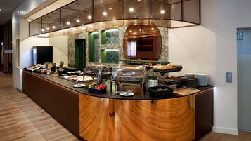A hotel breakfast bar with a variety of food options, a coffee machine, and a seating area.