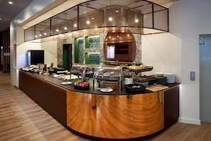 Un bufé de desayuno de hotel con diversas opciones de comida, una máquina de café y una zona de estar.