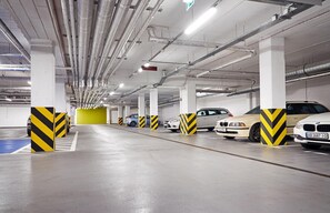 A multi-level underground parking garage with several cars parked, ventilation ducts, and yellow and black striped bollards. - B&B Hotel Lublin Centrum (Lublin)
