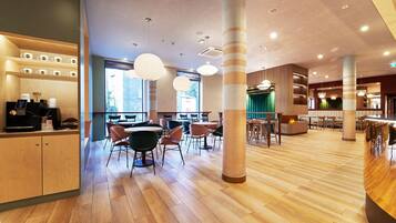 A modern cafe interior with wooden flooring, round tables, and chairs, and a coffee machine on the left.