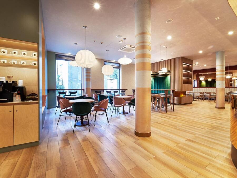 A modern cafe interior with wooden flooring, round tables, and chairs, and a coffee machine on the left.