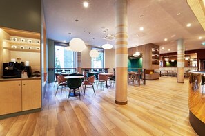 Interior moderno de una cafetería con suelo de madera, mesas y sillas redondas, y una máquina de café a la izquierda.