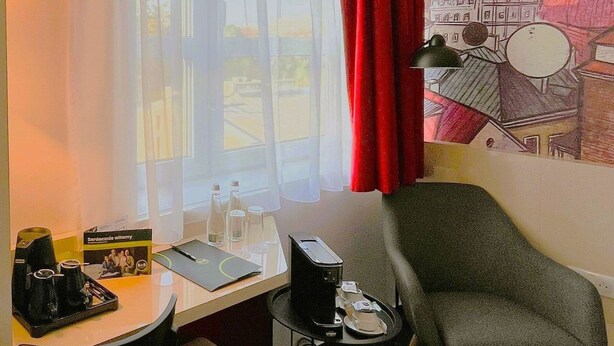 A hotel room with a desk, chair, and a small table with a lamp. - B&B Hotel Lublin Centrum (Lublin)