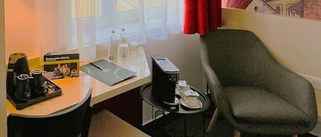 Quarto de hotel com escrivaninha, cadeira e uma pequena mesa com abajur.