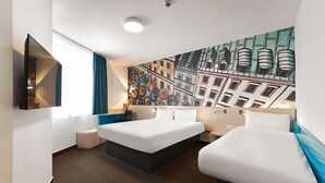 A hotel room with two beds, a large window with curtains, a wall-mounted TV, and a colorful mural. - B&B Hotel Lublin Centrum (Lublin)