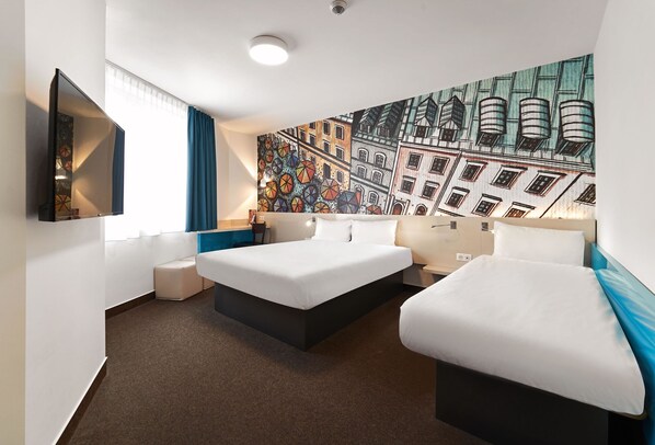 Habitación de hotel con dos camas, un ventanal grande con cortinas, un televisor montado en la pared y un mural colorido.