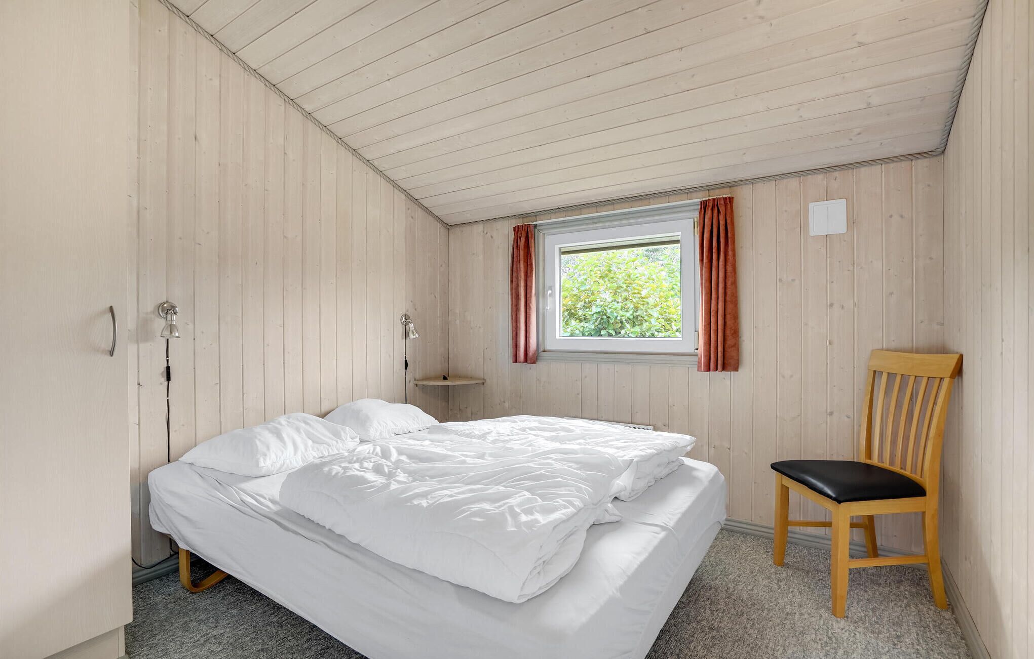 A single bed with white bedding in a room with wooden walls and a sloped ceiling.