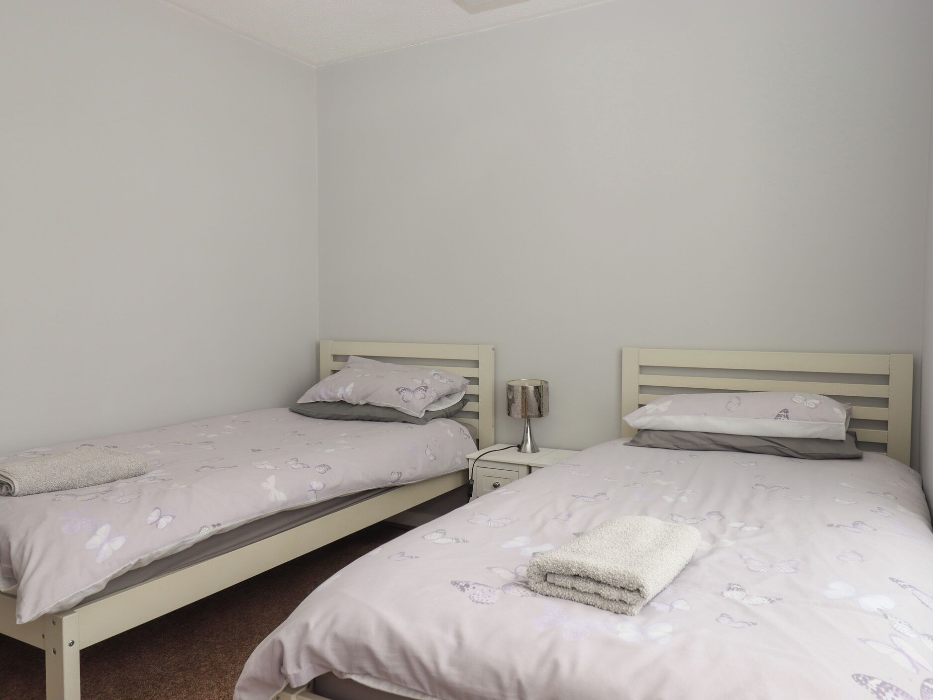 Een slaapkamer met twee eenpersoonsbedden, elk voorzien van een nachtkastje en een lamp.