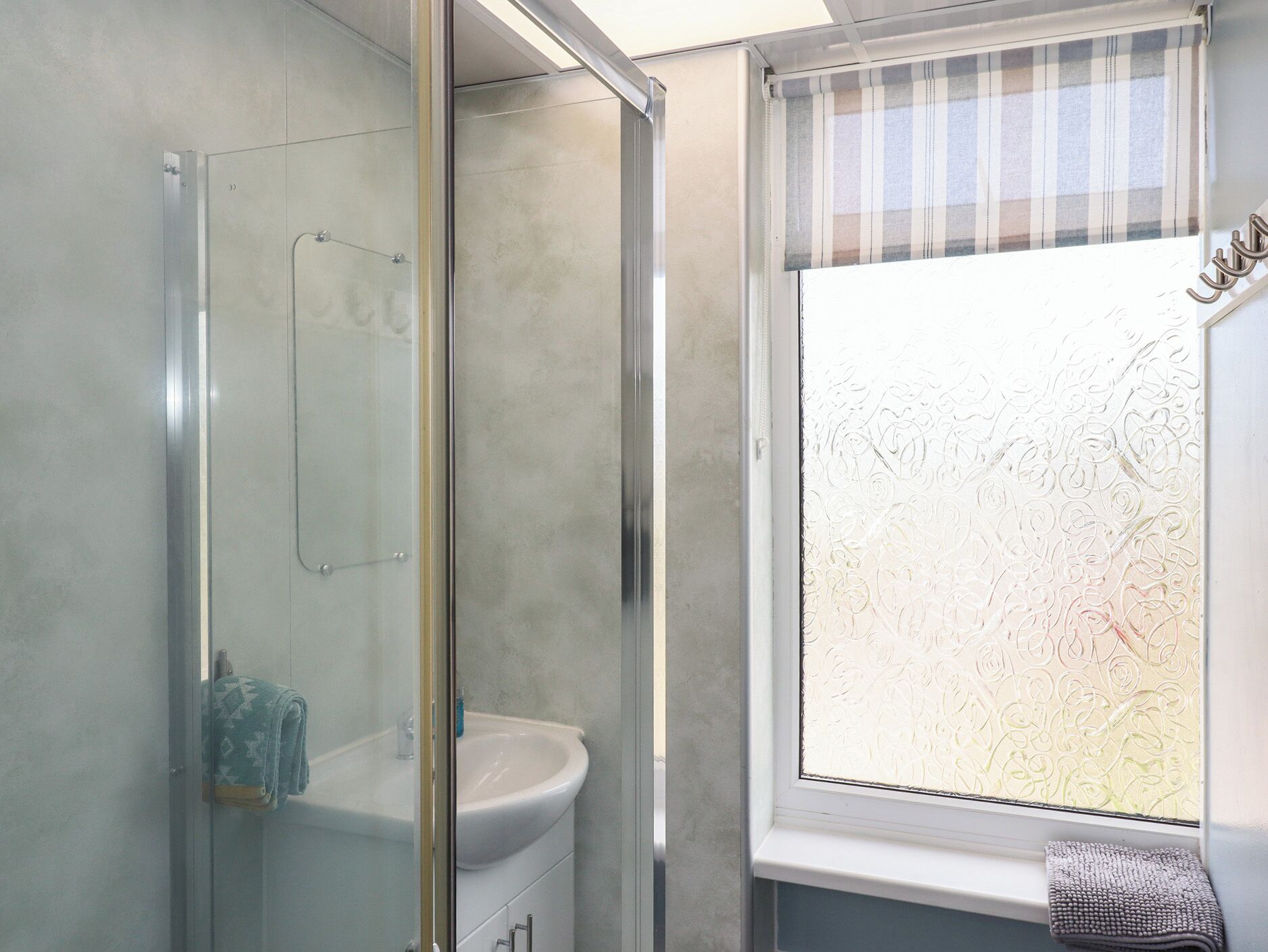 A bathroom with a glass shower enclosure, a white sink, and a window with frosted glass.