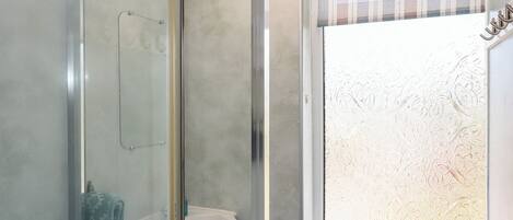 A bathroom with a glass shower enclosure, a white sink, and a window with frosted glass.