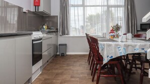 Une cuisine compacte dotée d’appareils électroménagers modernes, un coin repas avec une table dressée pour deux personnes et une fenêtre avec des rideaux.