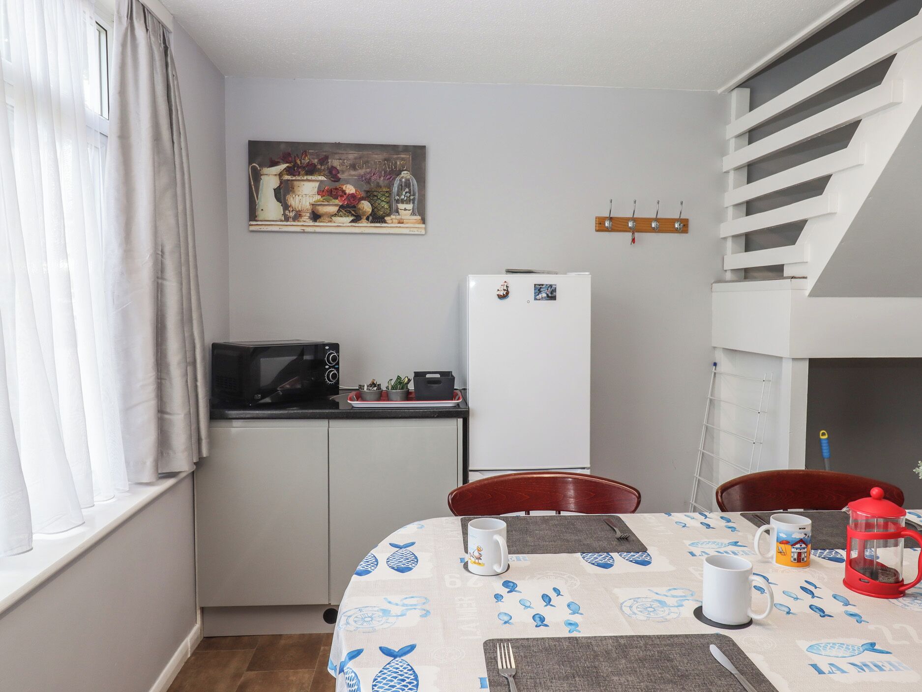 Eine kompakte Küche mit Mikrowelle, Kühlschrank und Esstisch, gedeckt mit einer Tischdecke und Besteck.