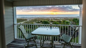 A balcony with a table and chairs, overlooking a beach with a sunset view. - Atlantic Sunrise ~ Oceanfront, Beachfront, Pools (Tybee Island)