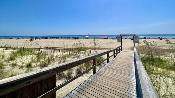 A wooden boardwalk leading to a beach with umbrellas and beachgoers. - Atlantic Sunrise ~ Oceanfront, Beachfront, Pools (Tybee Island)