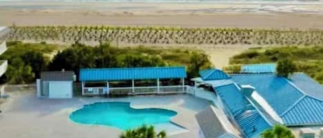 A beachfront property with a swimming pool, a covered area, and a beach in the background.