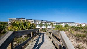 A wooden boardwalk leading to a beachfront hotel with multiple balconies and a clear blue sky. - Atlantic Sunrise ~ Oceanfront, Beachfront, Pools (Tybee Island)