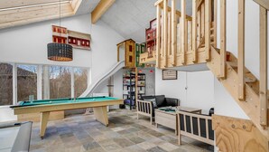 Een knus interieur met een biljarttafel, een trap met houten leuningen, en een vide met opslagplanken.