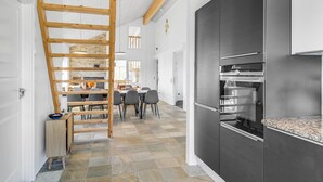 Een moderne keuken met een inbouwoven, een eethoek met een houten ladder en een vloer van stenen tegels.