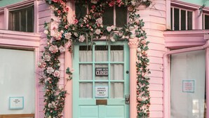 Un edificio rosa con puerta color turquesa, decoraciones florales y un letrero que dice 'Cerrado'.
