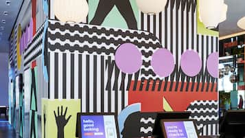 A modern interior with a check-in kiosk, a large abstract mural, and hanging paper lanterns.